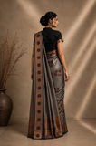 Woman wearing a traditional saree with a brown and black border against a beige background