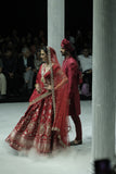 RED BROCADE DOUBLE LAYER LEHENGA PAIRED WITH A RED DUPION EMBROIDERED BLOUSE, RED EMBROIDERED DUPATTA, AND RED EMBROIDERED NET VEIL. (4 PCS)