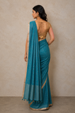 Woman wearing a teal saree with a beige blouse against a neutral background