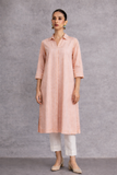 A SOFT PEACH TUNIC SHAPED IN FLUID SIMPLICITY, BALANCING STRUCTURE AND UNDERSTATED ELEGANCE