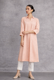 A SOFT PEACH TUNIC SHAPED IN FLUID SIMPLICITY, BALANCING STRUCTURE AND UNDERSTATED ELEGANCE