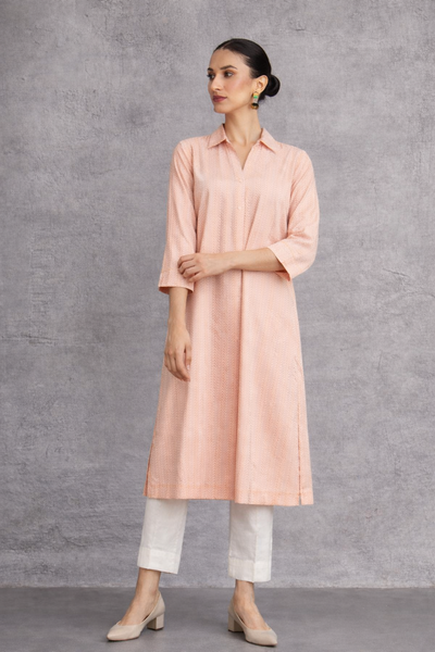 A SOFT PEACH TUNIC SHAPED IN FLUID SIMPLICITY, BALANCING STRUCTURE AND UNDERSTATED ELEGANCE
