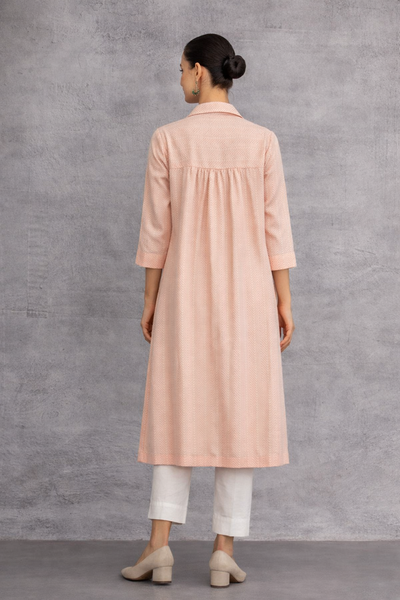 A SOFT PEACH TUNIC SHAPED IN FLUID SIMPLICITY, BALANCING STRUCTURE AND UNDERSTATED ELEGANCE
