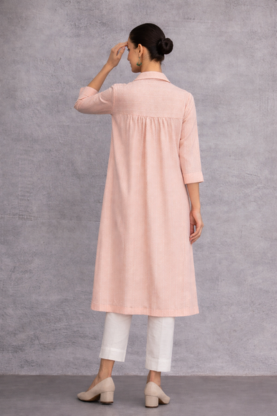 A SOFT PEACH TUNIC SHAPED IN FLUID SIMPLICITY, BALANCING STRUCTURE AND UNDERSTATED ELEGANCE