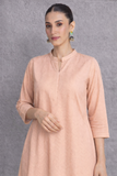 A SOFT PEACH TUNIC MARKED BY CLEAN LINES AND GENTLE MOVEMENT