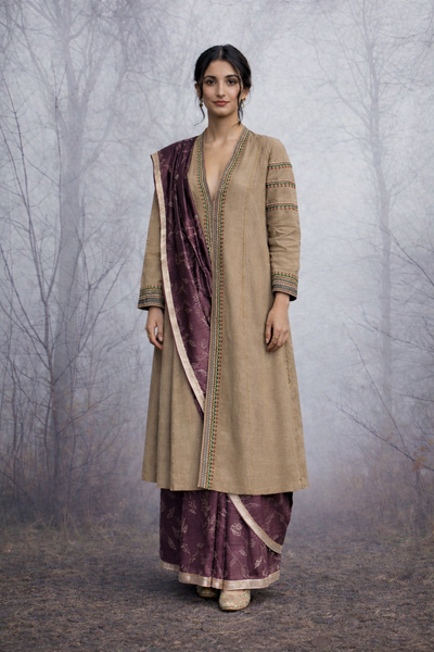 A LINEN JACKET LAYERED OVER A BROWN TUSSAR SAREE, BLENDING STRUCTURE WITH SOFT DRAPE.