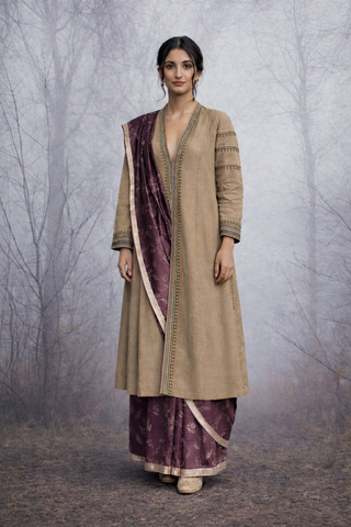 A LINEN JACKET LAYERED OVER A BROWN TUSSAR SAREE, BLENDING STRUCTURE WITH SOFT DRAPE.