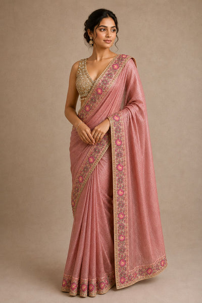 Woman wearing a pink saree with intricate patterns on a beige background