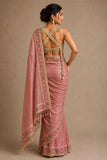 Woman wearing a pink saree with intricate patterns on a beige background