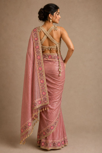 Woman wearing a pink saree with intricate patterns on a beige background