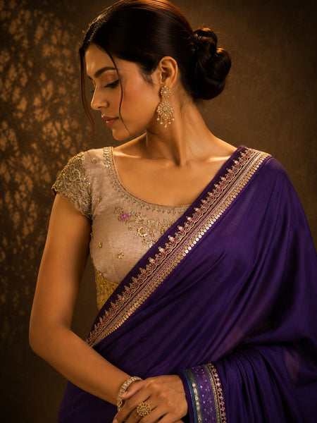 Woman wearing a traditional purple saree with intricate designs against a dark background