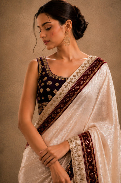 Woman wearing a traditional saree with intricate patterns on a beige background