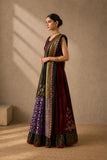 A woman models a traditional Indian anarkali gown with a matching dupatta. The dress features a deep maroon bodice, a dark green skirt with purple floral patterns, and ornate gold and silver embroidery along the borders.