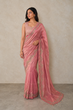 Woman wearing a pink saree with intricate designs against a neutral background